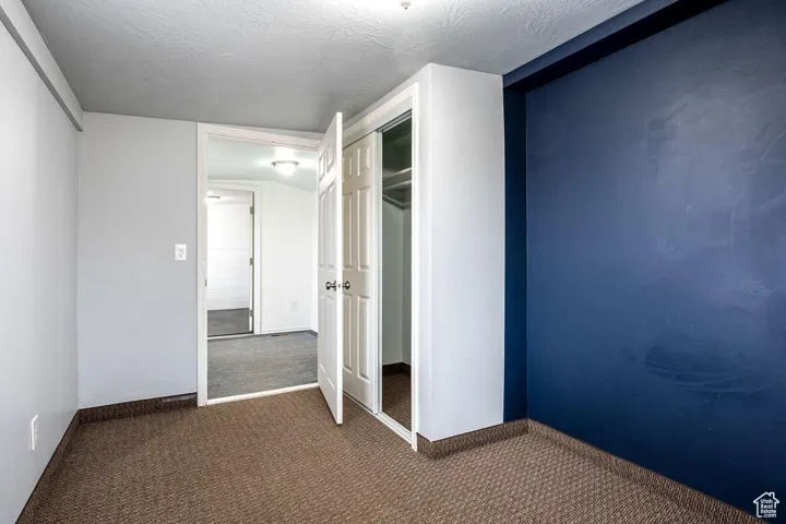 Unfurnished bedroom featuring carpet, a closet, a textured ceiling, and baseboards