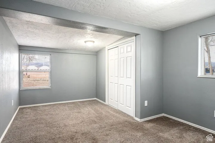 Unfurnished bedroom featuring carpet floors, a closet, a textured ceiling, and baseboards