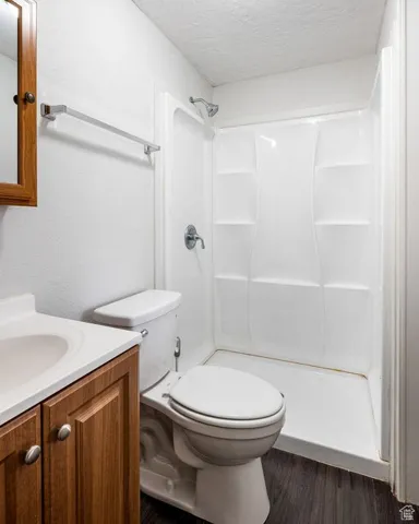 Full bathroom featuring toilet, a textured ceiling, vanity, wood finished floors, and walk in shower