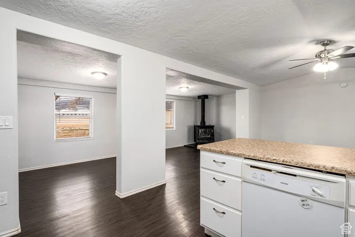 Kitchen with a wood stove, white dishwasher, white cabinetry, and dark wood-style flooring
