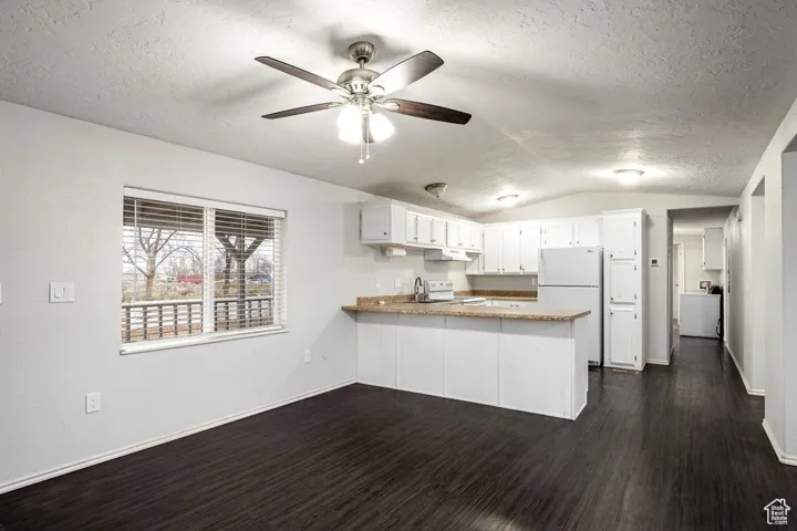 Kitchen featuring dark wood finished floors, stove, freestanding refrigerator, vaulted ceiling, and a peninsula