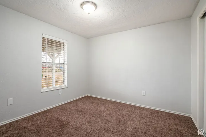 Carpeted spare room with a textured ceiling and baseboards