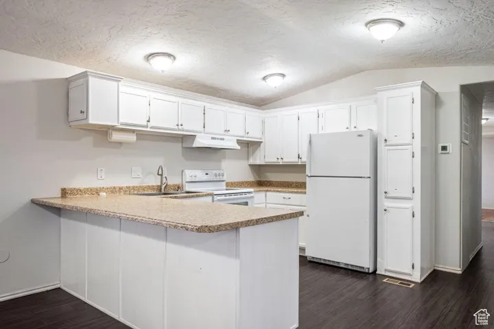 Kitchen featuring white appliances, a peninsula, vaulted ceiling, under cabinet range hood, and a sink