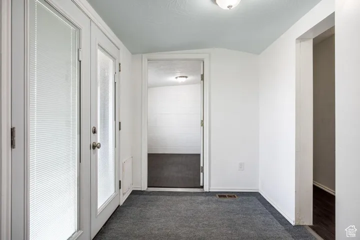 Hall featuring french doors, lofted ceiling, dark carpet, a textured ceiling, and baseboards