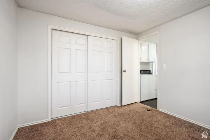 Unfurnished bedroom featuring dark colored carpet, a closet, a textured ceiling, separate washer and dryer, and baseboards