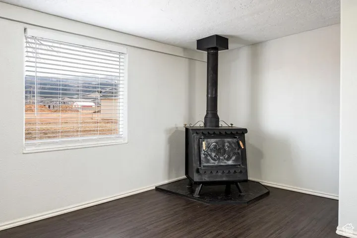 Interior details with a wood stove, a textured ceiling, baseboards, and wood finished floors
