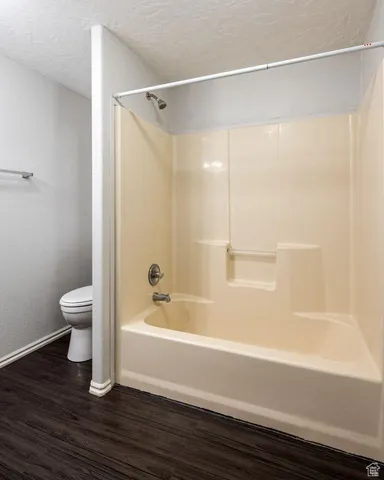 Bathroom featuring toilet, shower / bath combination, a textured ceiling, and wood finished floors