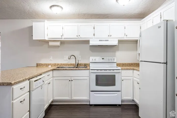 Kitchen with white appliances, a sink, white cabinets, and under cabinet range hood