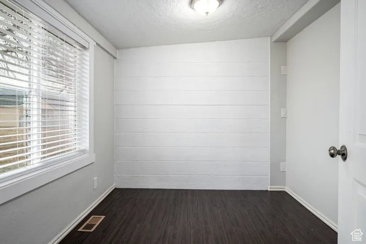 Empty room with baseboards, a textured ceiling, visible vents, and dark wood-type flooring