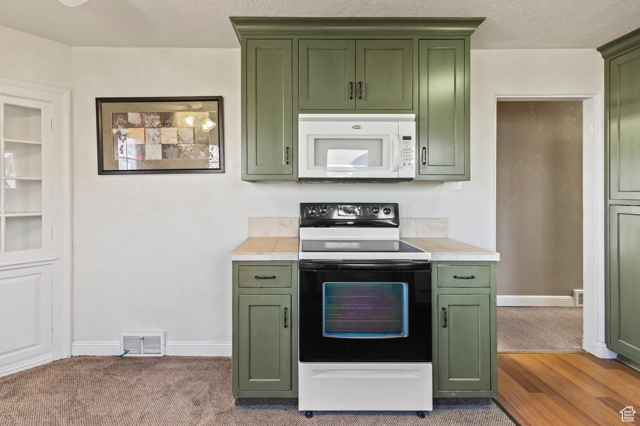 Kitchen with electric range, visible vents, green cabinets, white microwave, and tile counters