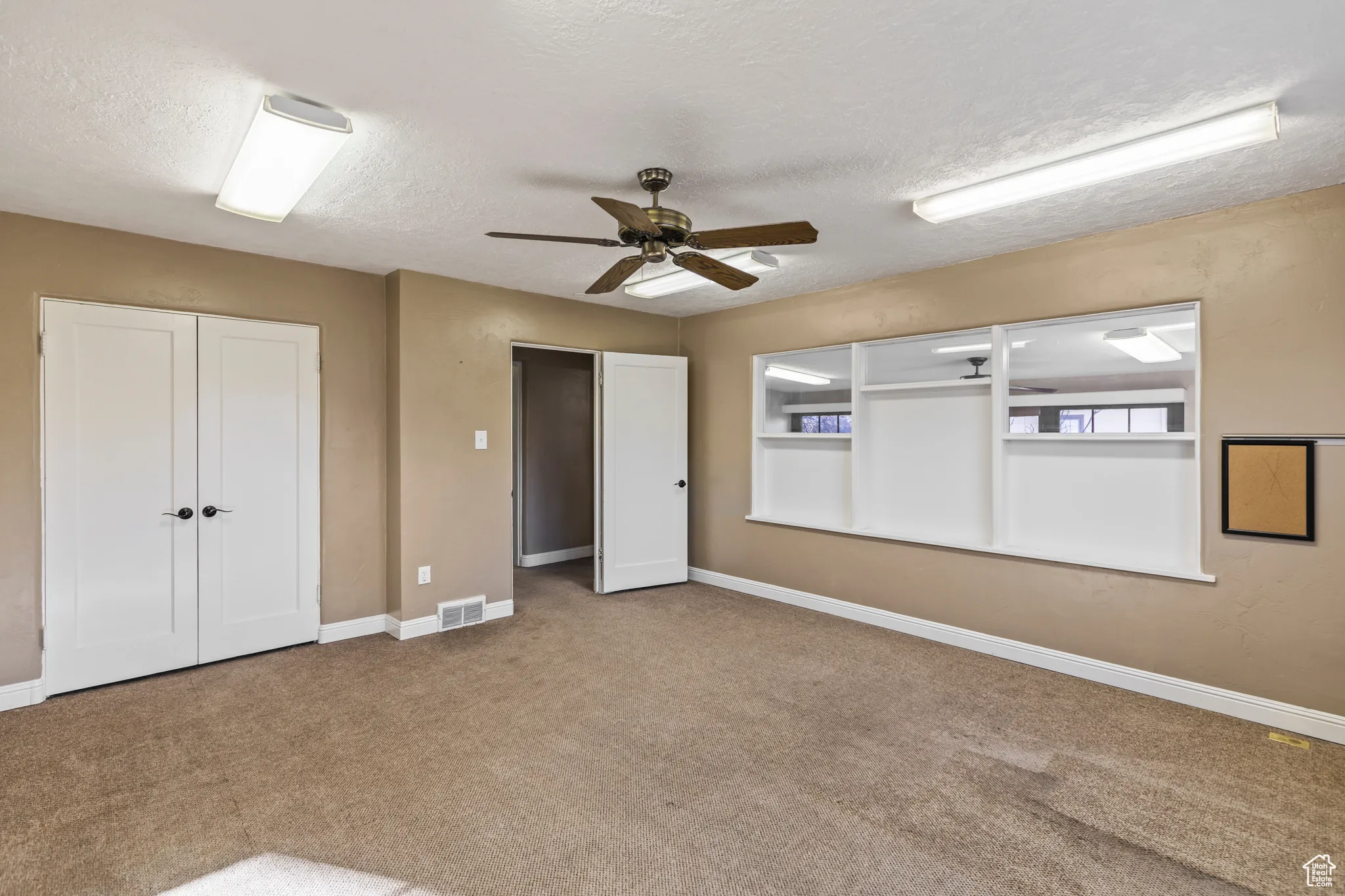 Carpeted empty room with visible vents, baseboards, a textured ceiling, and a ceiling fan