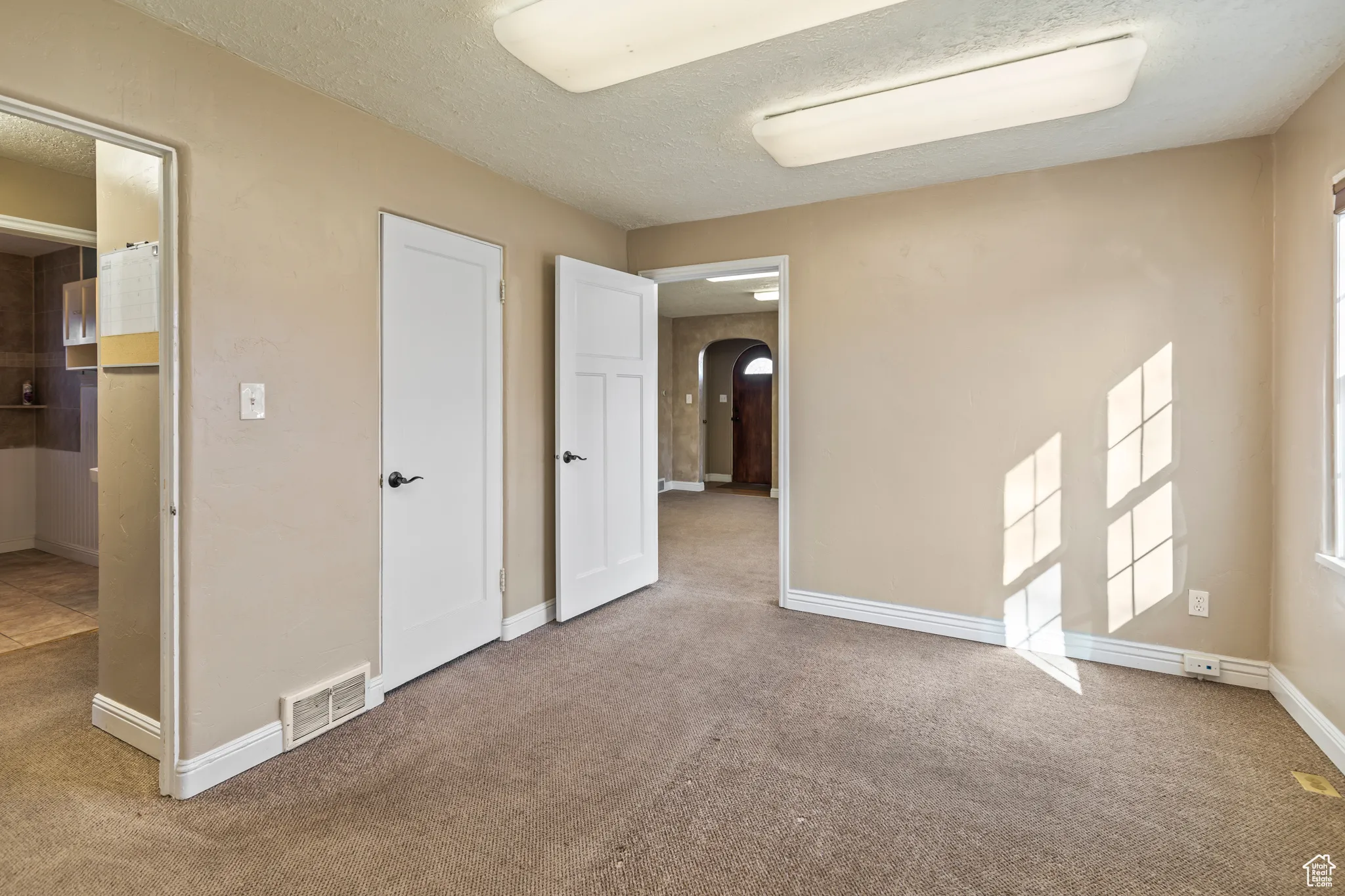 Unfurnished bedroom with baseboards, visible vents, carpet floors, arched walkways, and a textured ceiling