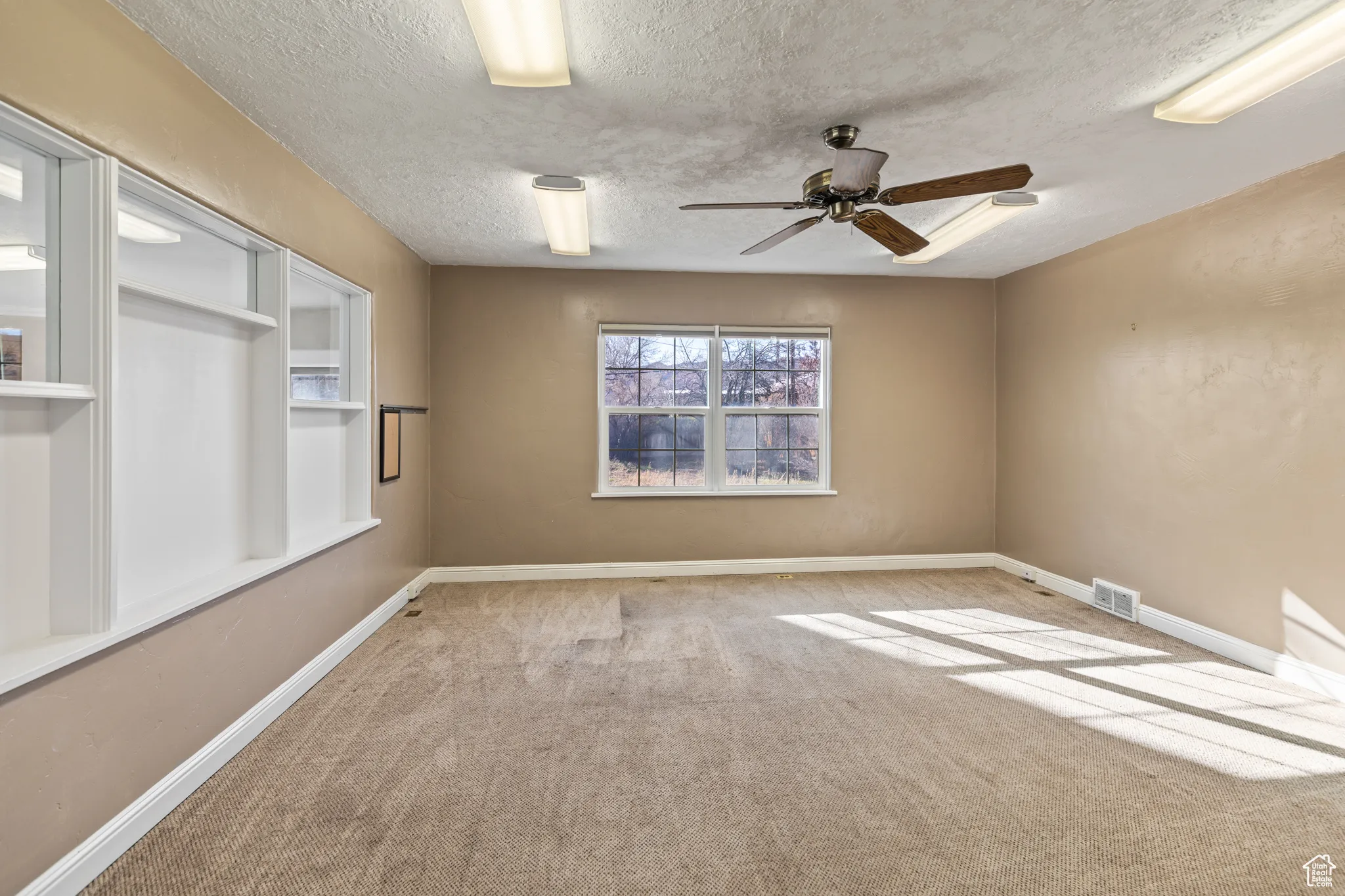 Spare room with a textured ceiling, carpet, visible vents, and baseboards