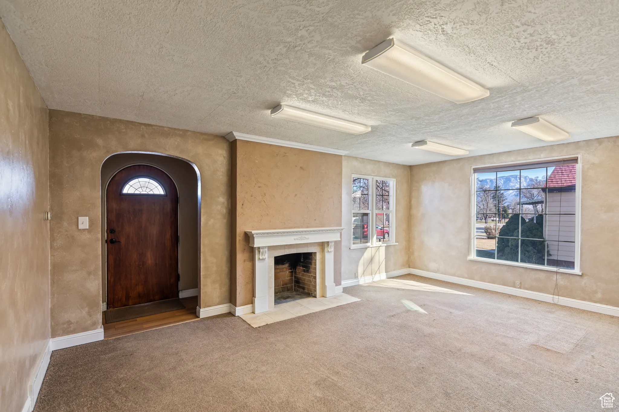 Unfurnished living room with baseboards, arched walkways, carpet floors, and a fireplace with flush hearth