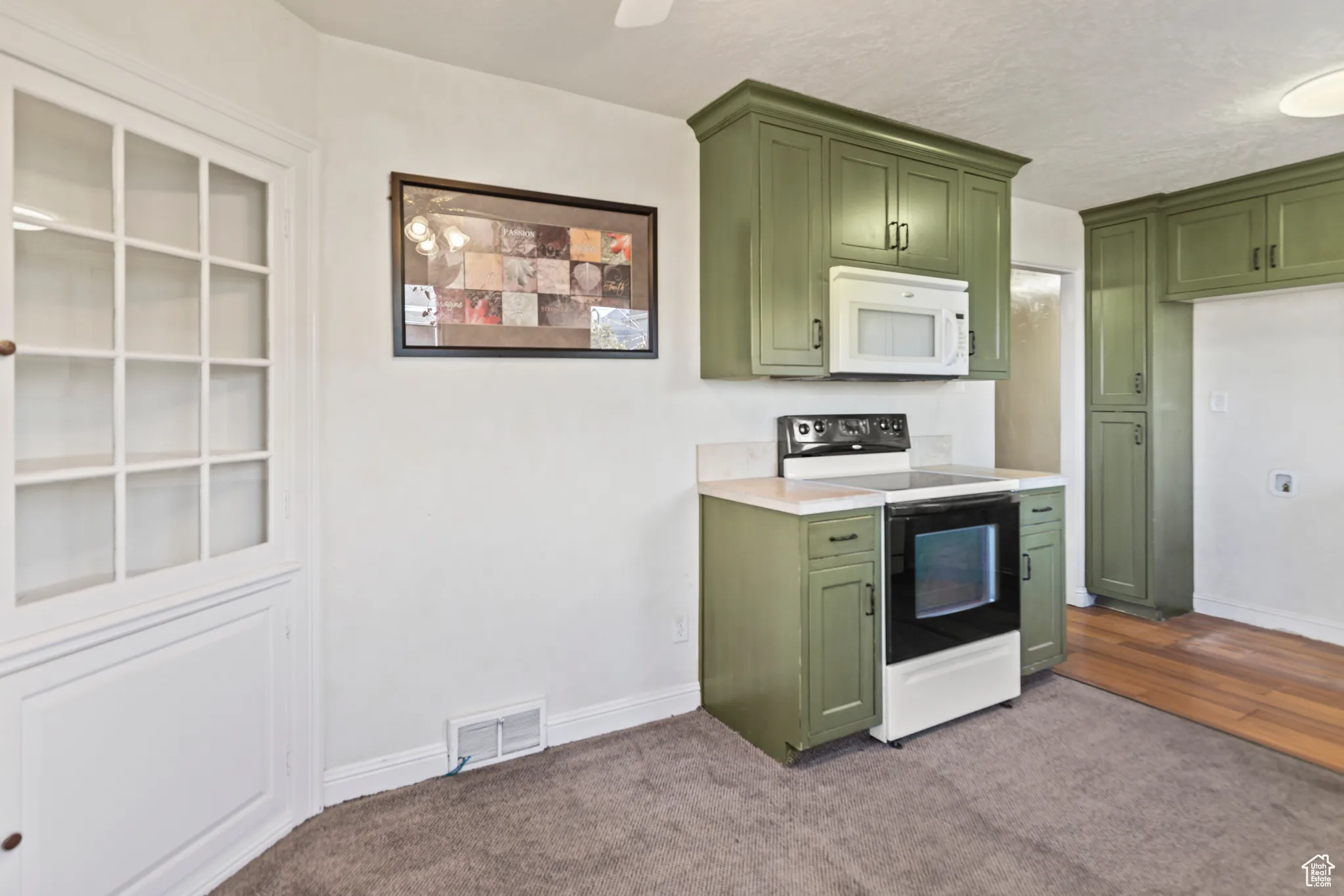 Kitchen with white microwave, range with electric cooktop, green cabinets, carpet, and light countertops