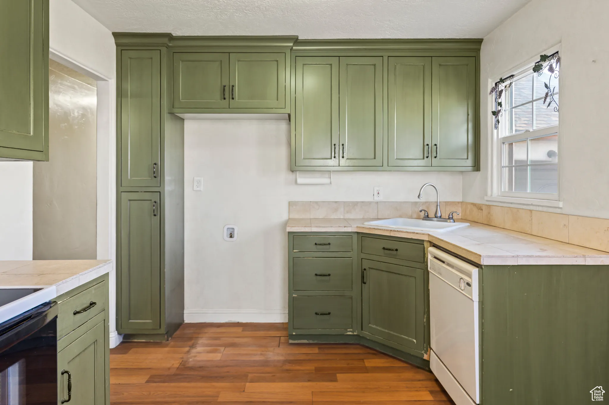Kitchen with tile countertops, dishwasher, green cabinets, and a sink