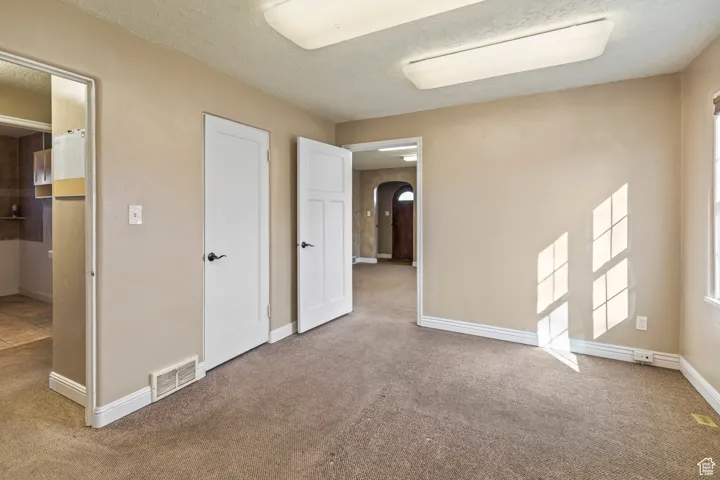 Unfurnished bedroom with baseboards, visible vents, carpet floors, arched walkways, and a textured ceiling