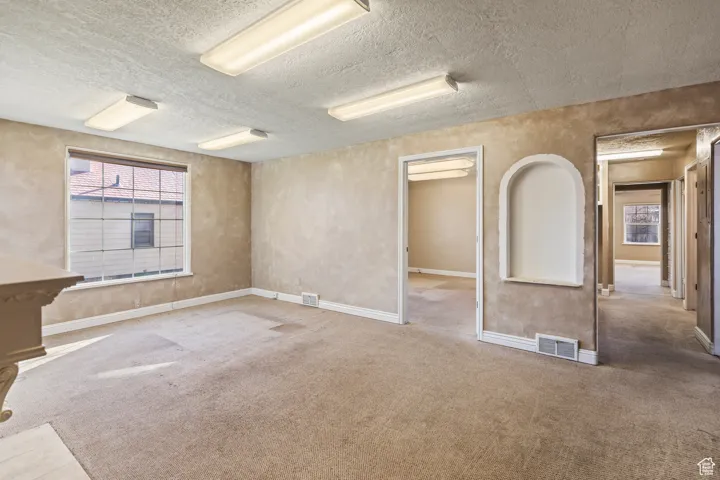 Unfurnished room featuring carpet flooring, baseboards, visible vents, and a textured ceiling