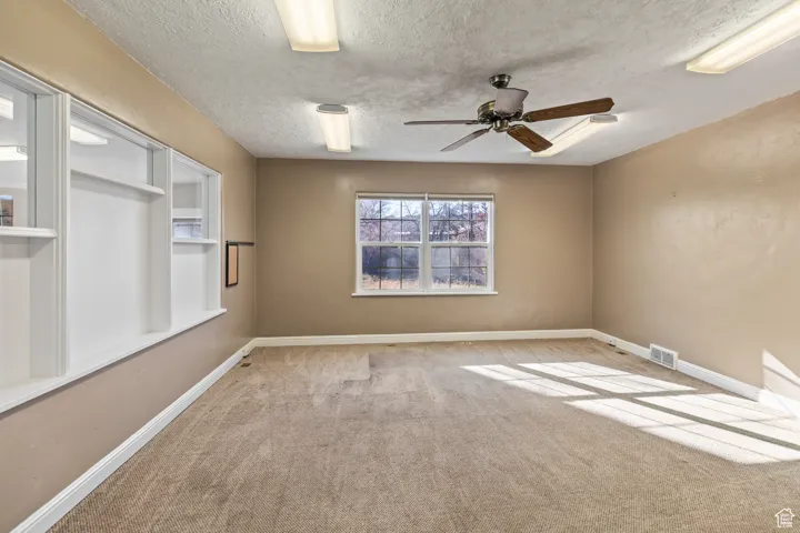 Spare room with a textured ceiling, carpet, visible vents, and baseboards