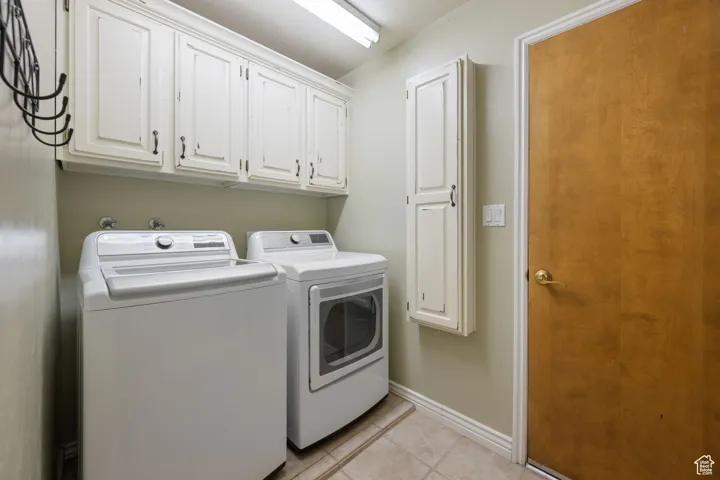 Clothes washing area with light tile patterned flooring, independent washer and dryer, cabinet space, and baseboards