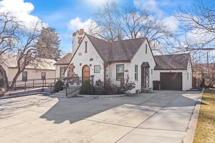 View of front of house with stucco siding, roof with shingles, concrete driveway, a garage, and a chimney