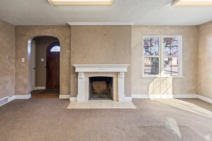 Unfurnished living room featuring a tiled fireplace, a textured ceiling, carpet floors, arched walkways, and baseboards