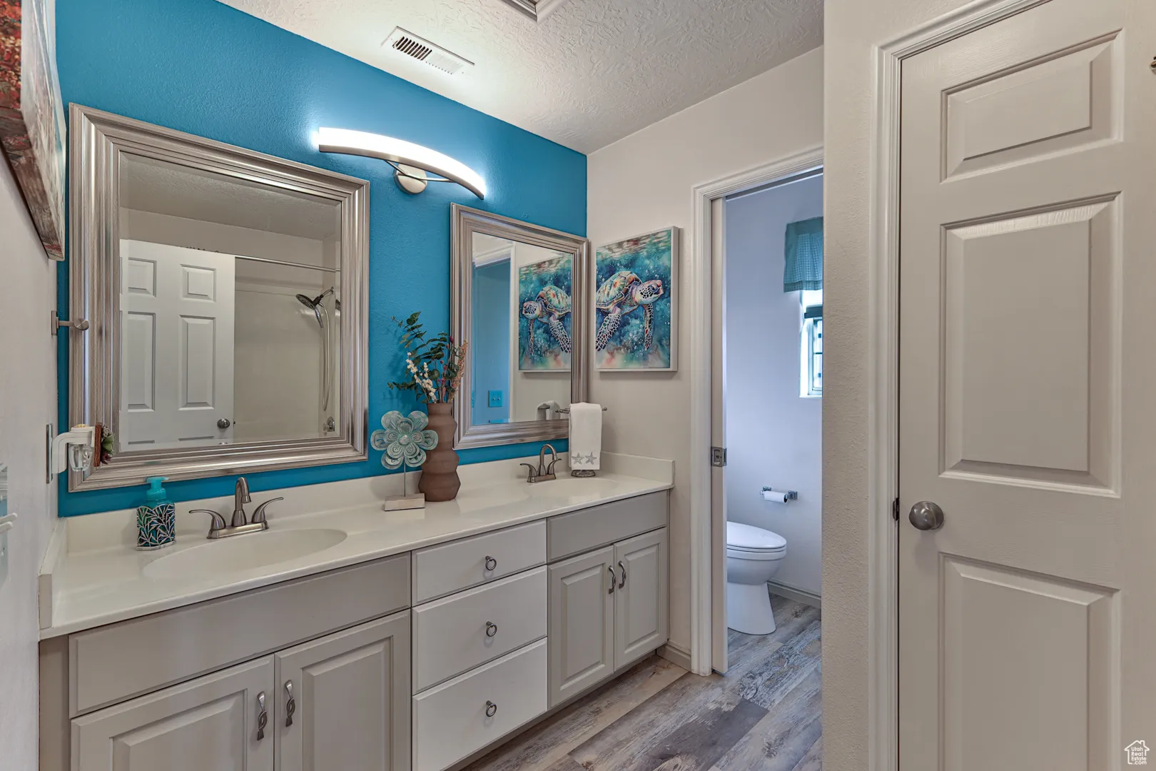 Bathroom featuring a textured ceiling, toilet, visible vents, and a sink