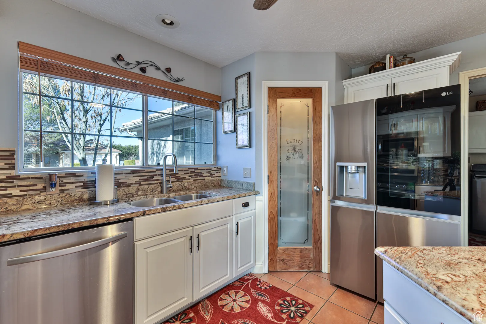 Kitchen featuring tasteful backsplash, light tile patterned floors, white cabinets, stainless steel appliances, and a sink