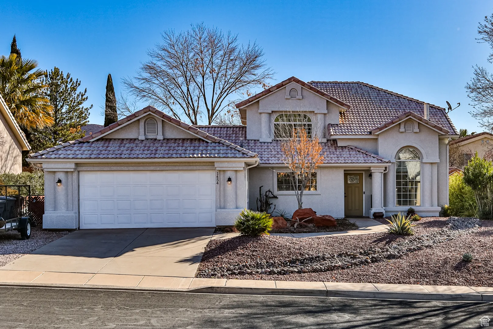 View of front facade featuring a tiled roof, an attached garage, driveway, and stucco siding