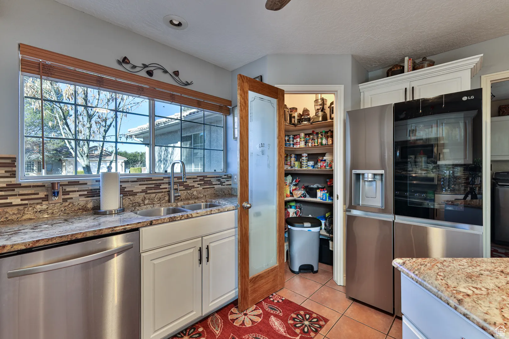 Kitchen with tasteful backsplash, light tile patterned floors, white cabinets, stainless steel appliances, and a sink