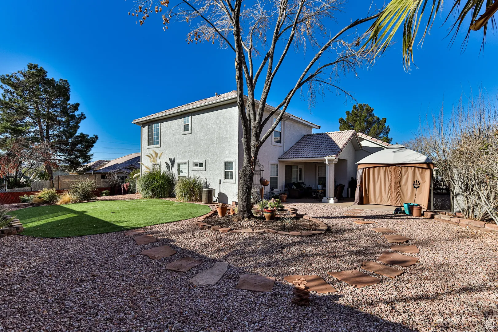 Rear view of property featuring stucco siding, a lawn, fence, an outdoor structure, and a patio area