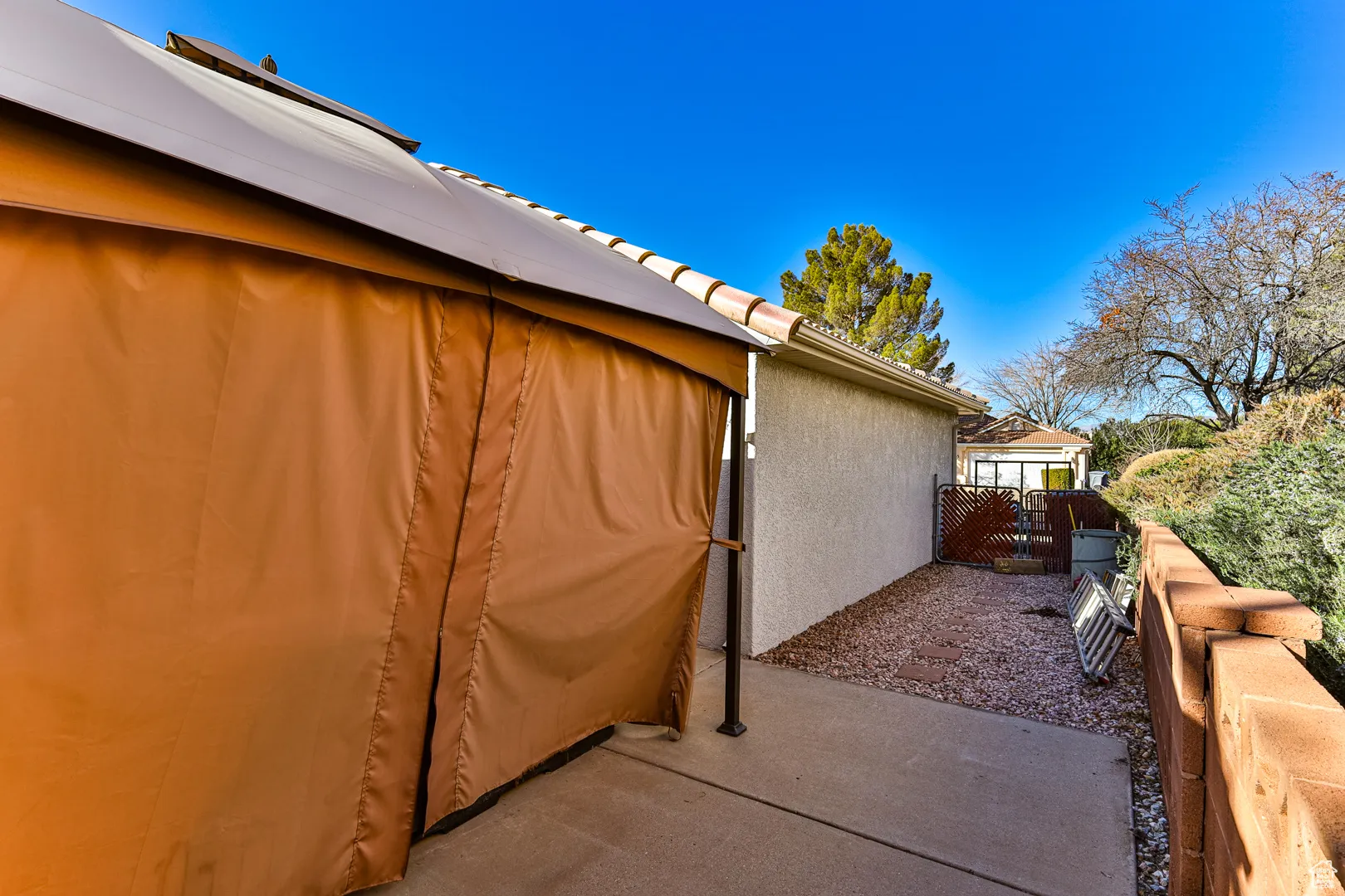 View of property exterior with stucco siding, a gate, a patio, fence, and a tiled roof