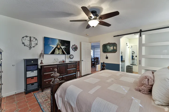 Bedroom with tile patterned flooring, ceiling fan, a textured ceiling, and a barn door