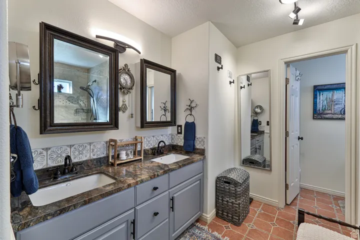 Full bath with tile patterned flooring, a textured ceiling, tiled shower, and a sink