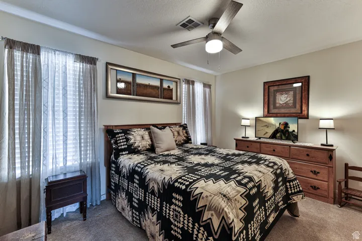 Bedroom with a ceiling fan, visible vents, carpet floors, and a textured ceiling