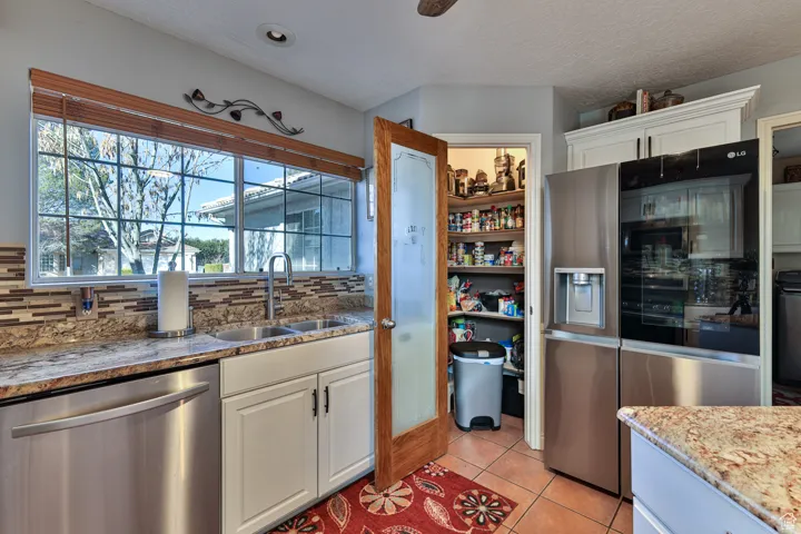 Kitchen with tasteful backsplash, light tile patterned floors, white cabinets, stainless steel appliances, and a sink
