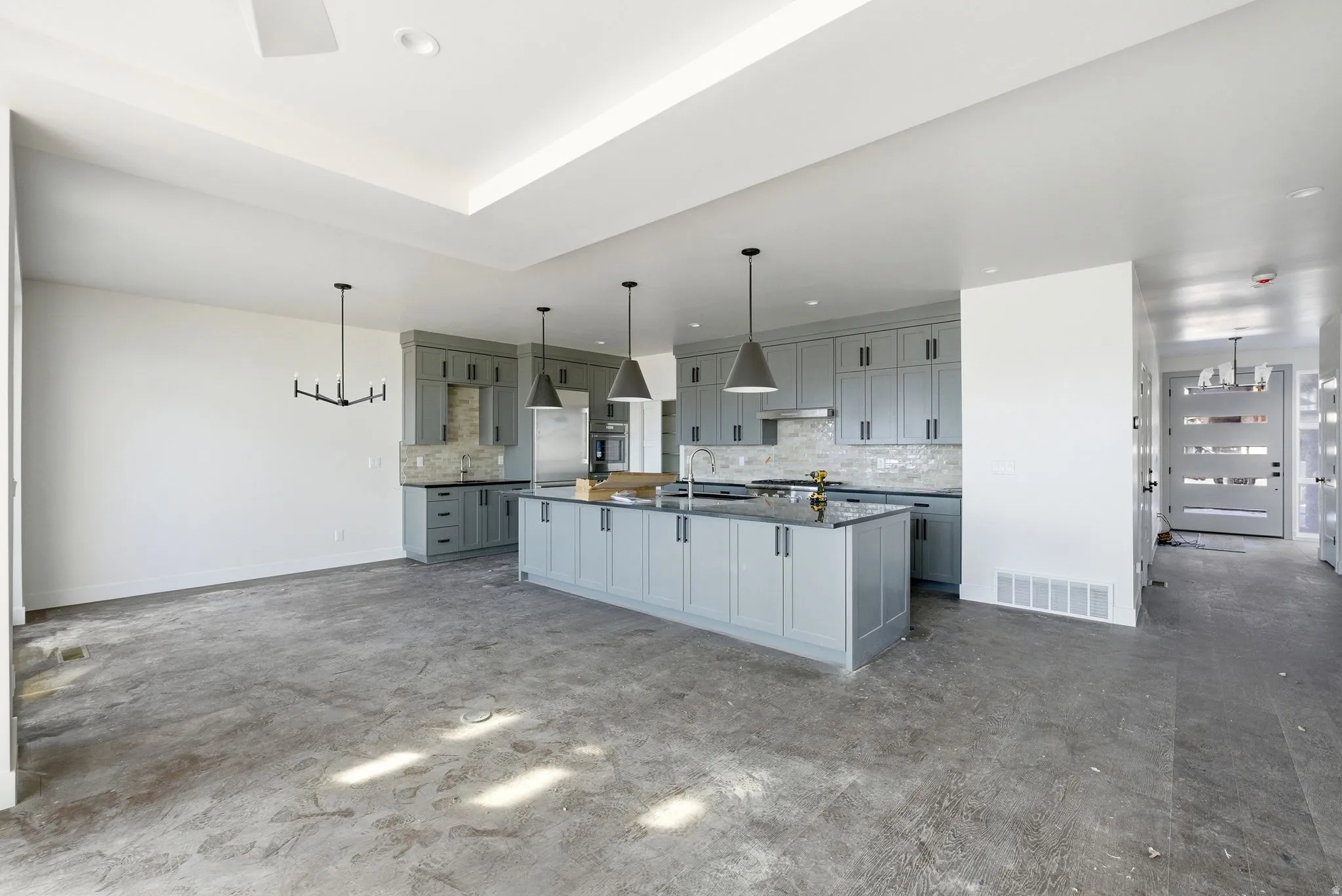 Kitchen with gray cabinetry, dark countertops, hanging lights, and a large island with sink