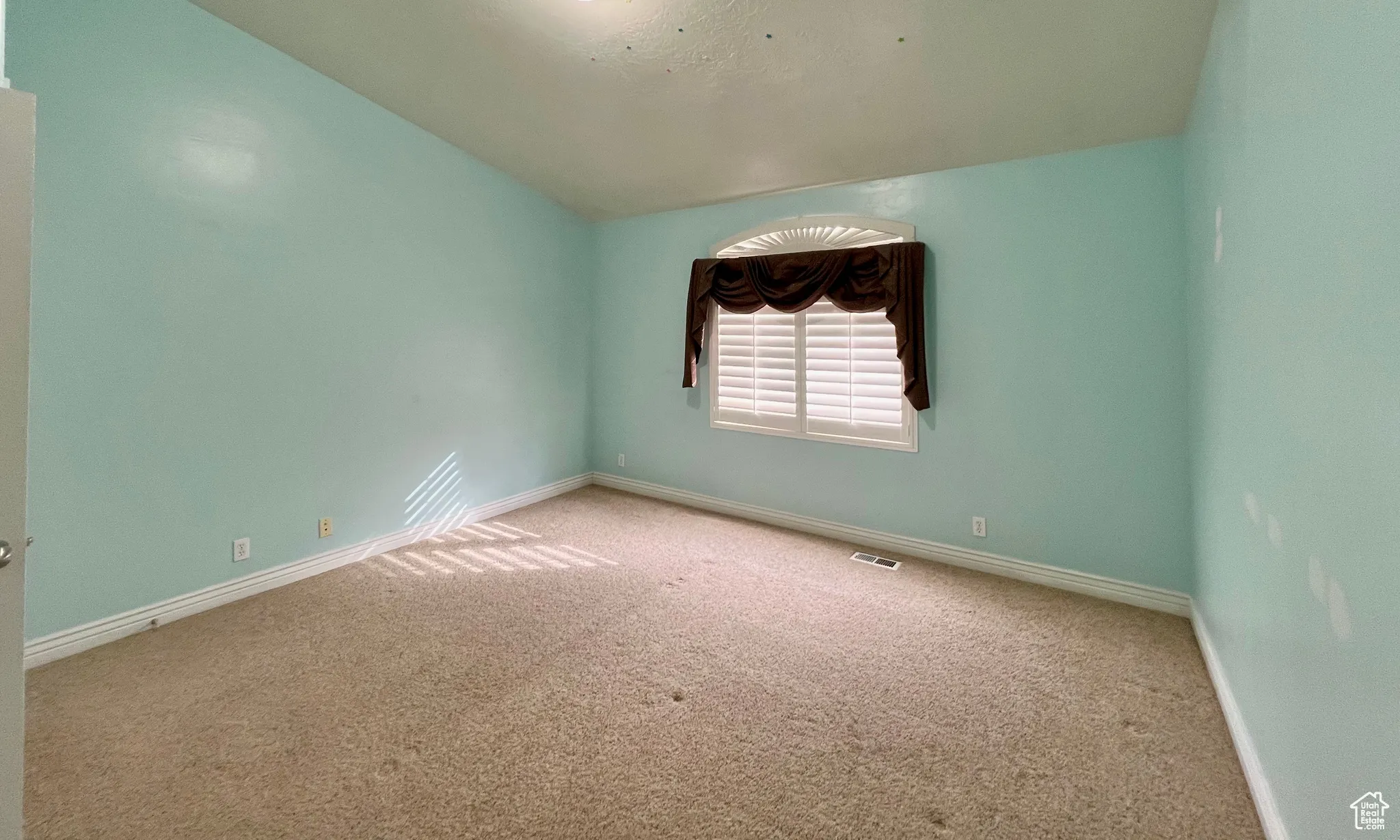 Carpeted empty room with visible vents, lofted ceiling, and baseboards