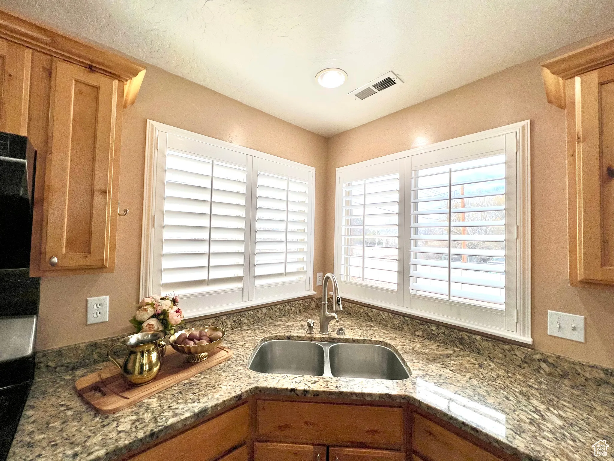 Kitchen featuring a sink, visible vents, stone countertops, and brown cabinetry