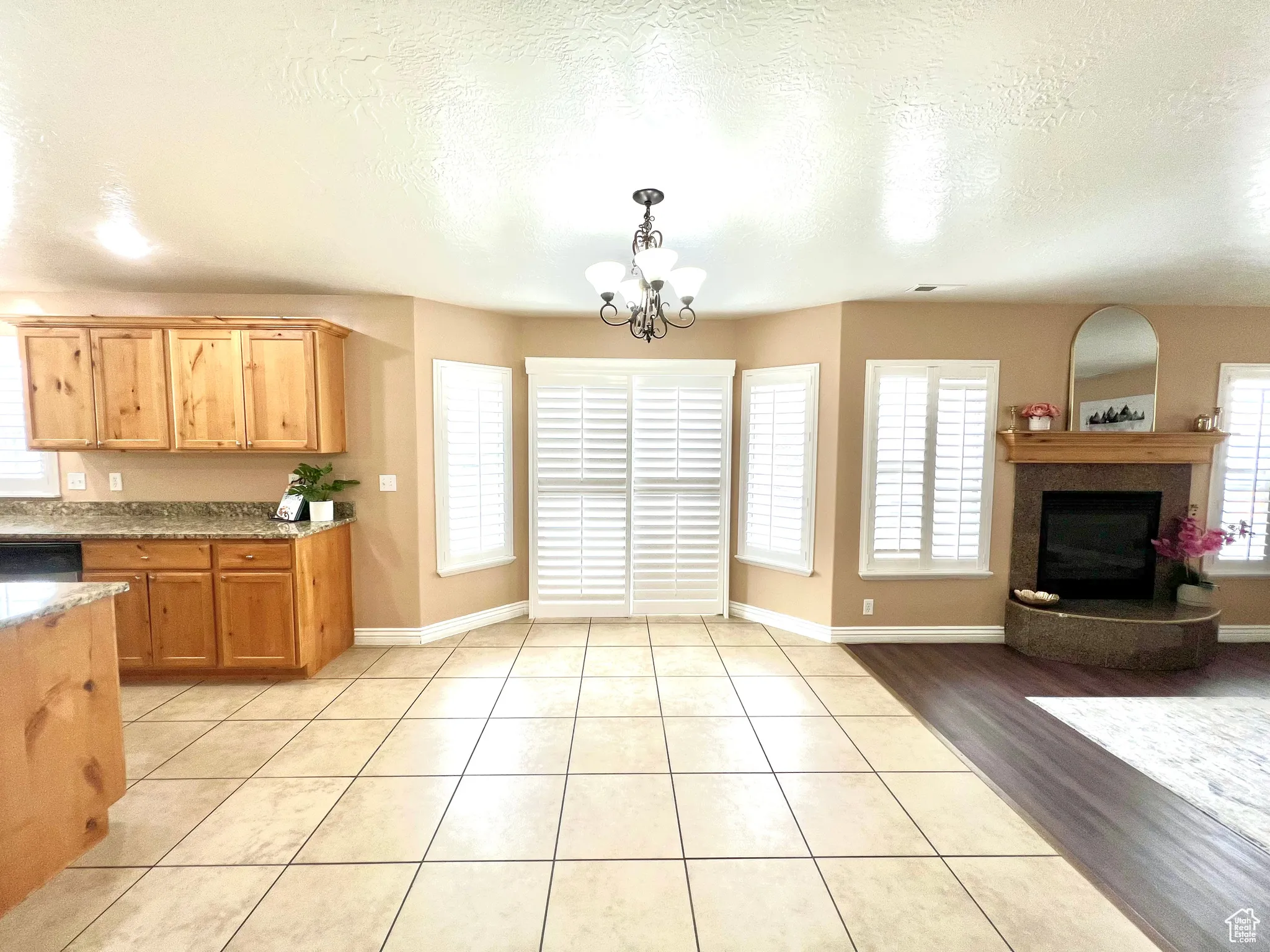 Kitchen featuring light stone countertops, an inviting chandelier, light tile patterned flooring, a fireplace with raised hearth, and hanging light fixtures