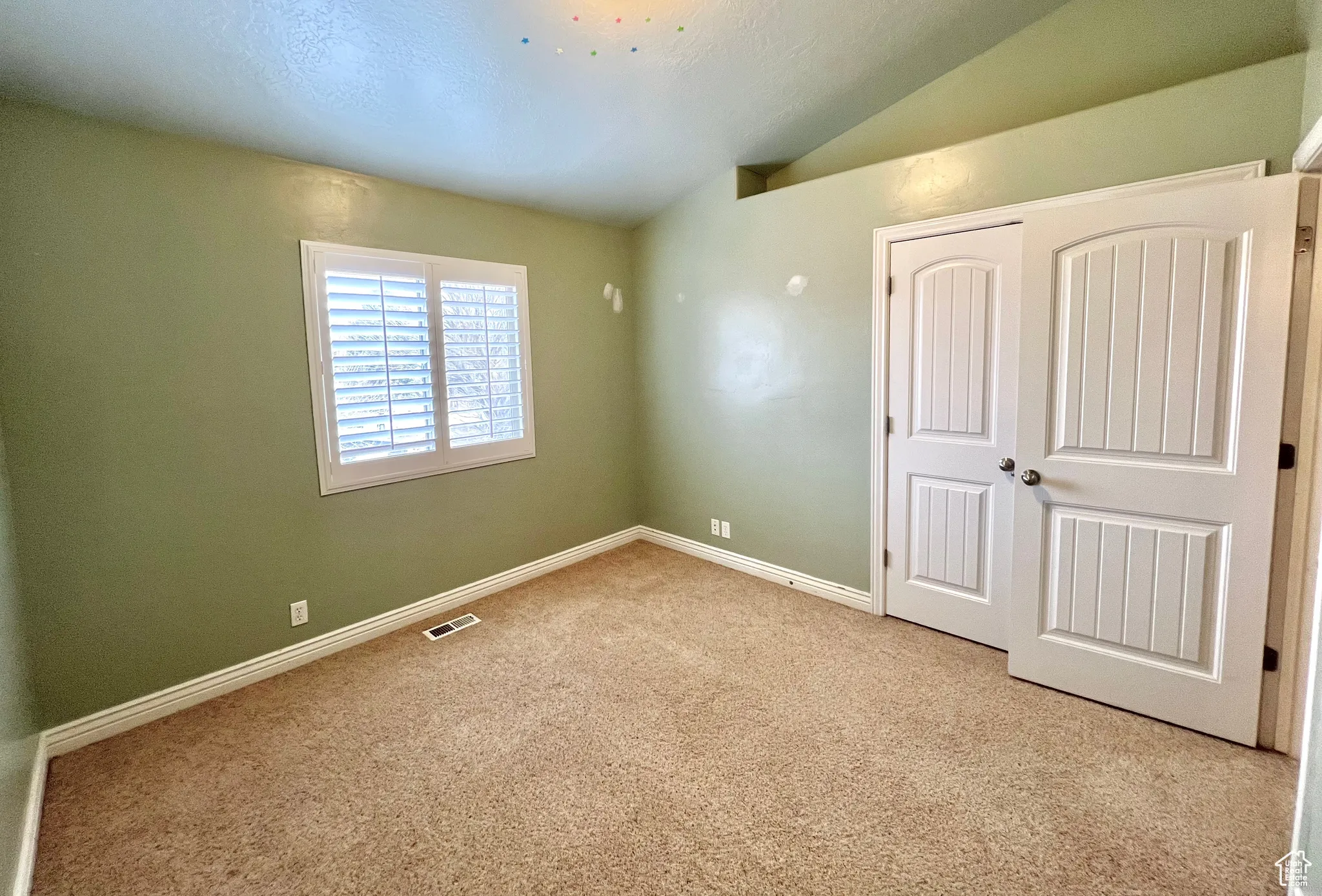 Unfurnished bedroom featuring carpet, baseboards, visible vents, lofted ceiling, and a closet