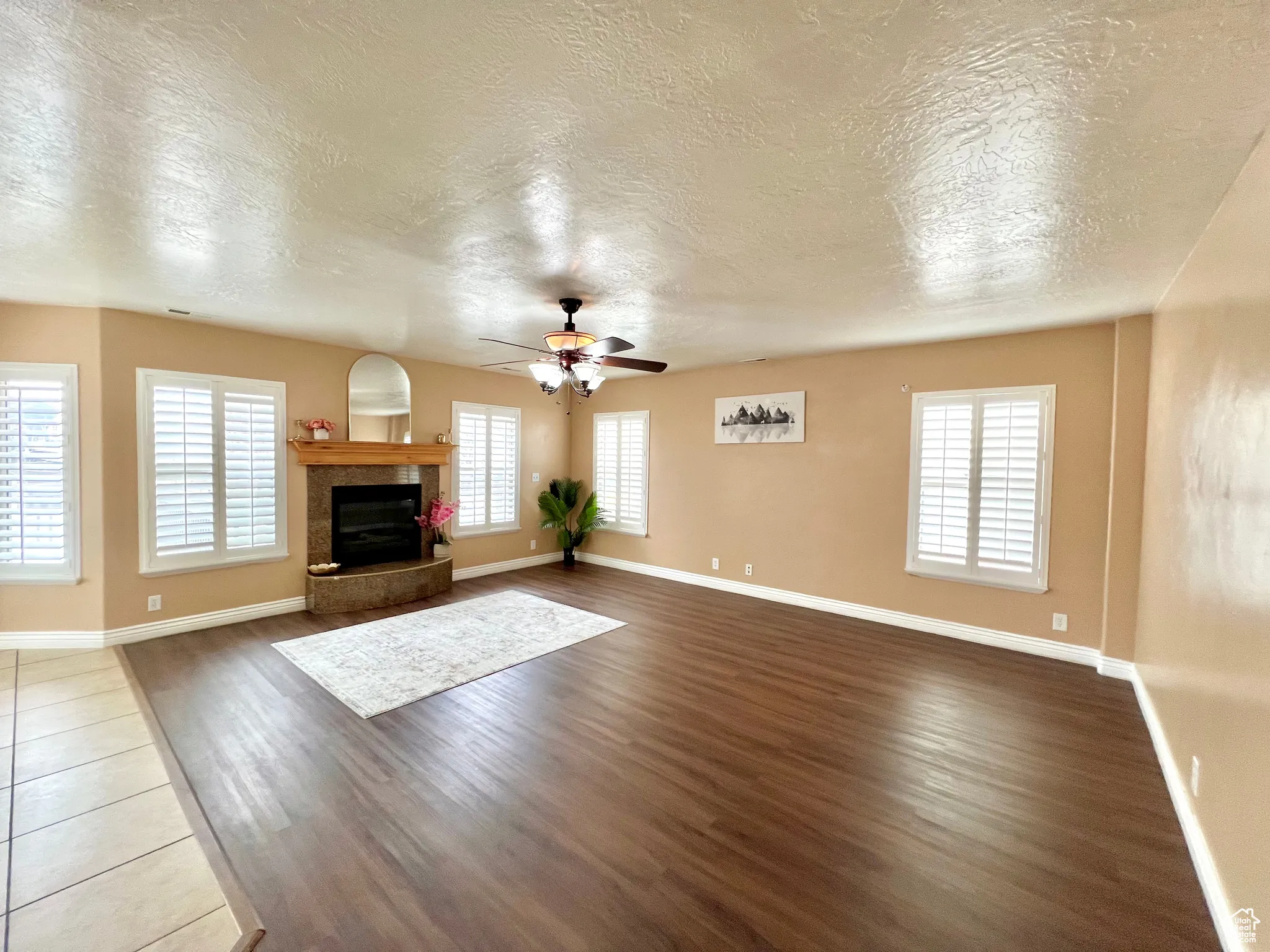 Unfurnished living room with baseboards, dark wood-type flooring, ceiling fan, and a tile fireplace