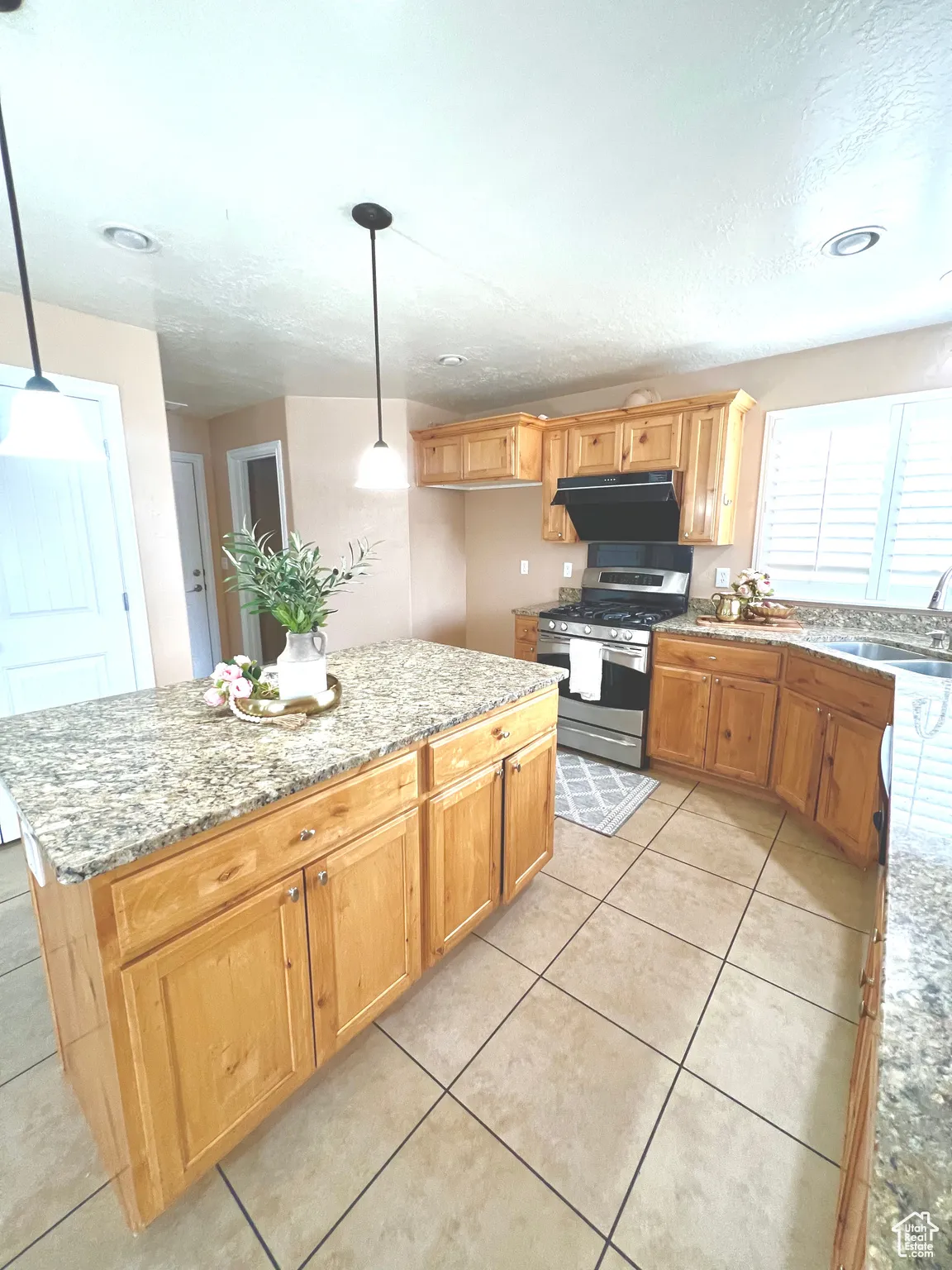 Kitchen featuring stainless steel gas range oven, light stone countertops, range hood, and a sink