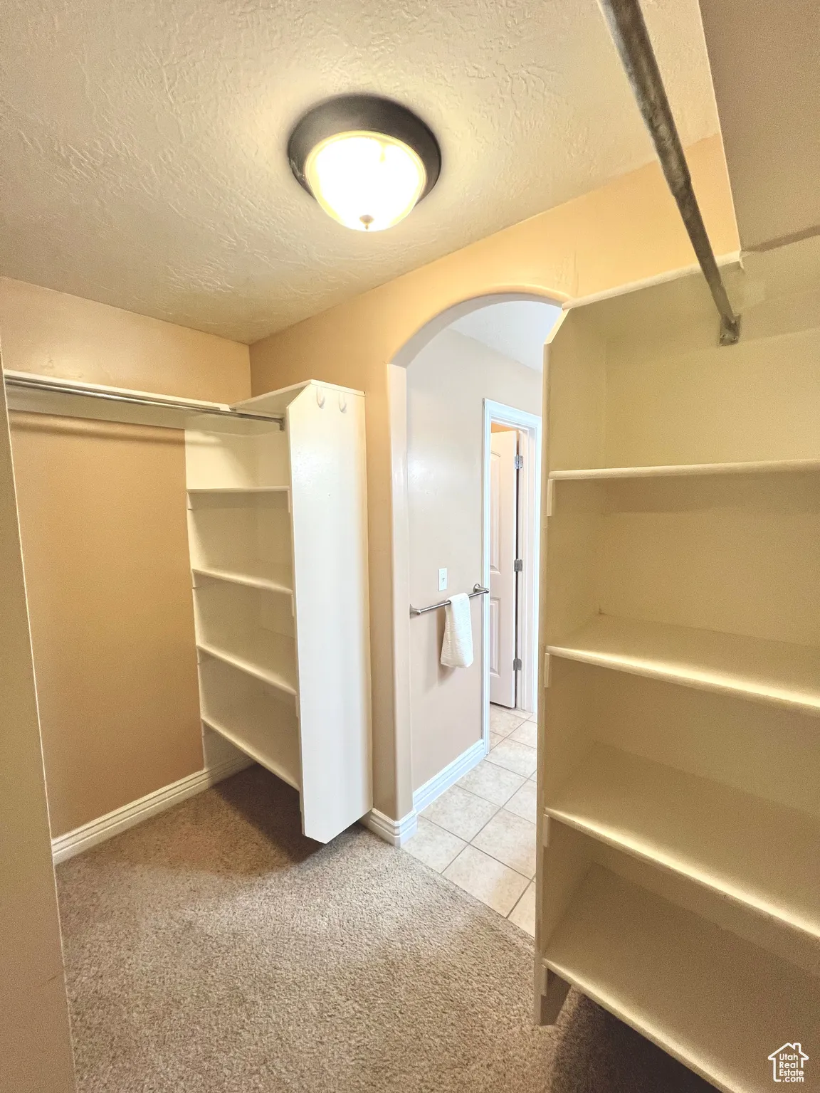 Walk in closet featuring light carpet, light tile patterned floors, and arched walkways