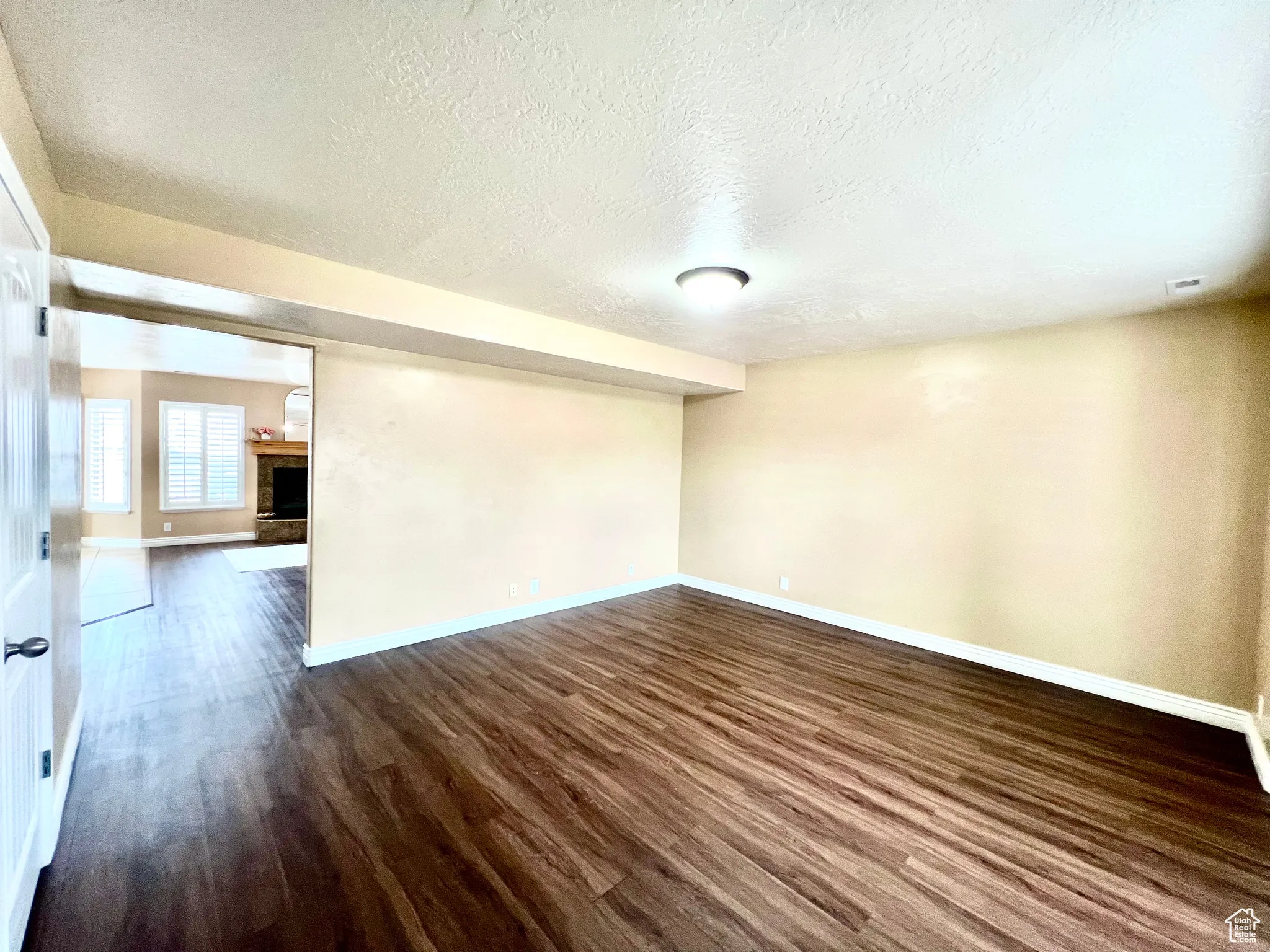 Spare room featuring visible vents, a fireplace with raised hearth, baseboards, a textured ceiling, and dark wood-style flooring