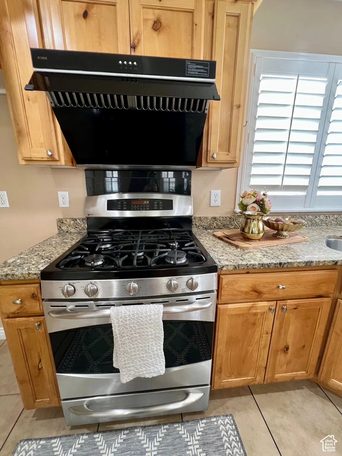 Kitchen featuring range hood, light stone counters, light tile patterned flooring, and gas stove