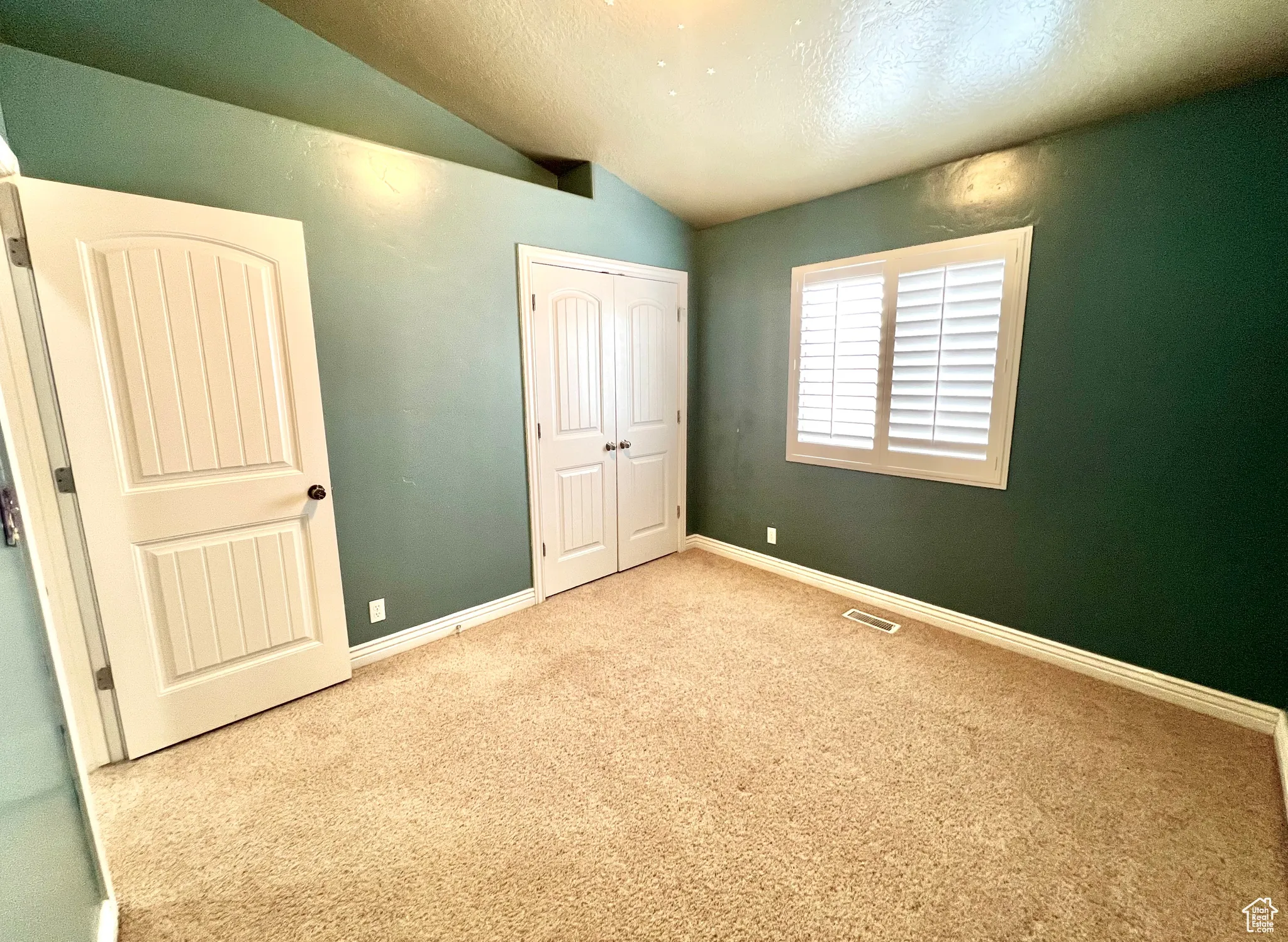 Unfurnished bedroom featuring visible vents, baseboards, carpet, lofted ceiling, and a closet