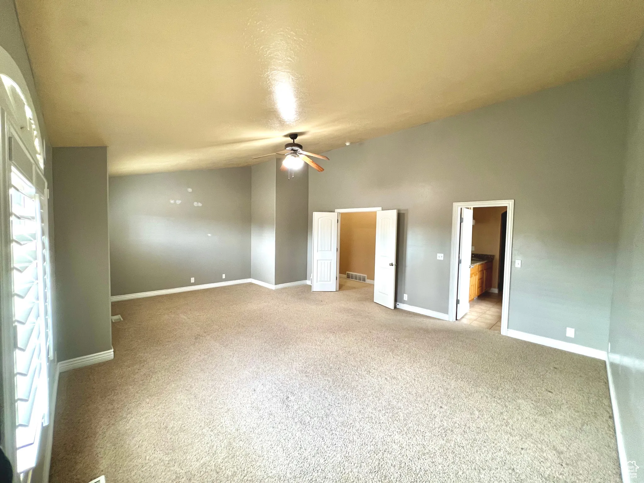 Unfurnished bedroom with visible vents, baseboards, vaulted ceiling, light carpet, and a ceiling fan