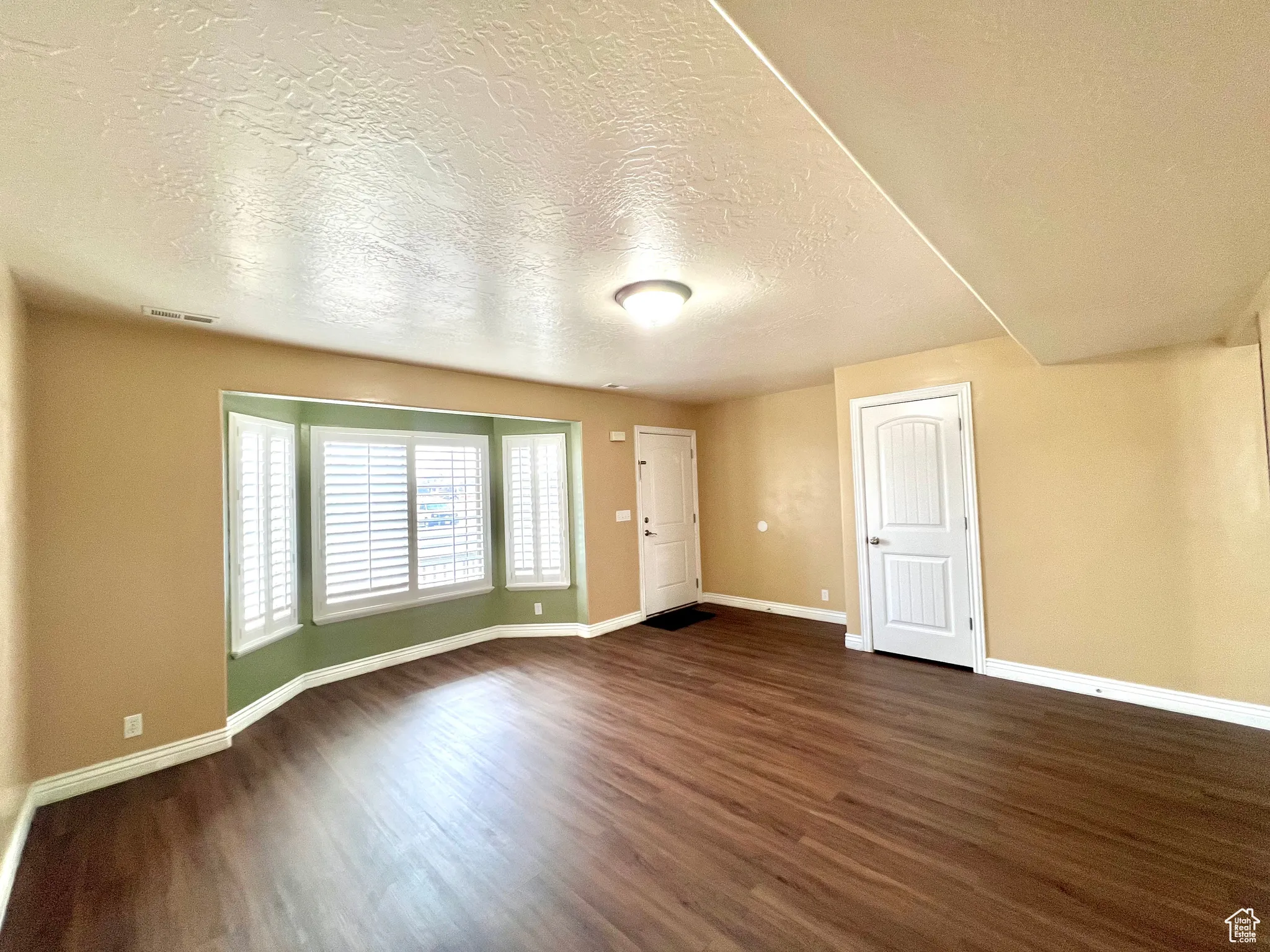 Empty room featuring dark wood finished floors, baseboards, visible vents, and a textured ceiling