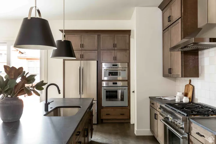 Kitchen with dark countertops, high quality appliances, wall chimney range hood, and a sink